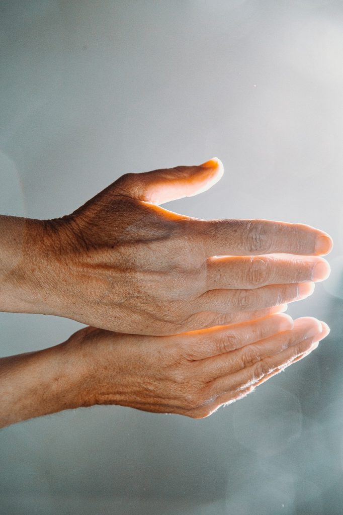 Hands lifted in prayer with sunlight symbolising faith.