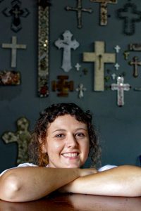 A young girl smiling - there are crosses on the wall behind her.